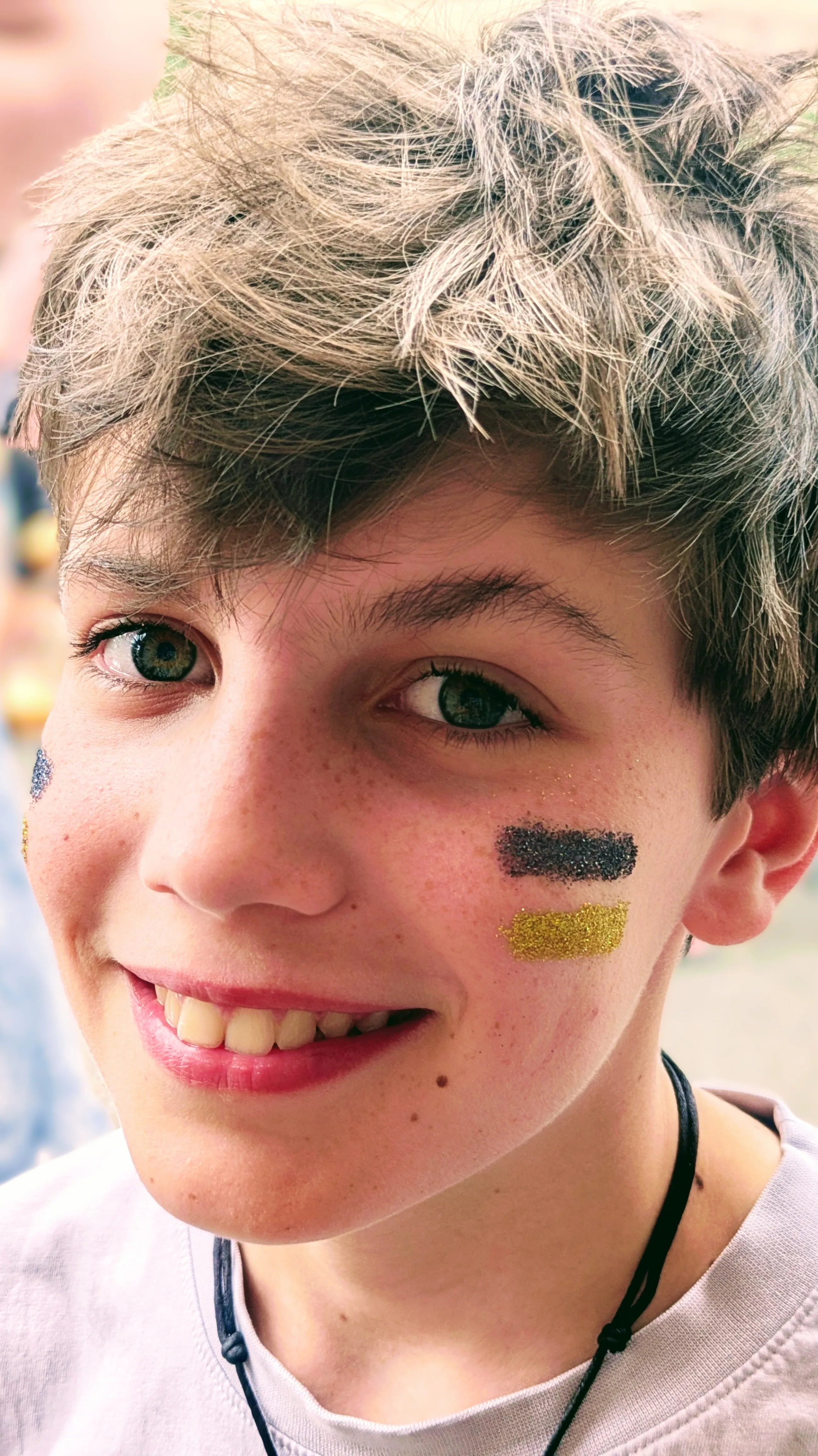 Maquillage paillet&eacute; noir et dor&eacute; en deux traits sur les joues d&rsquo;un adolescent